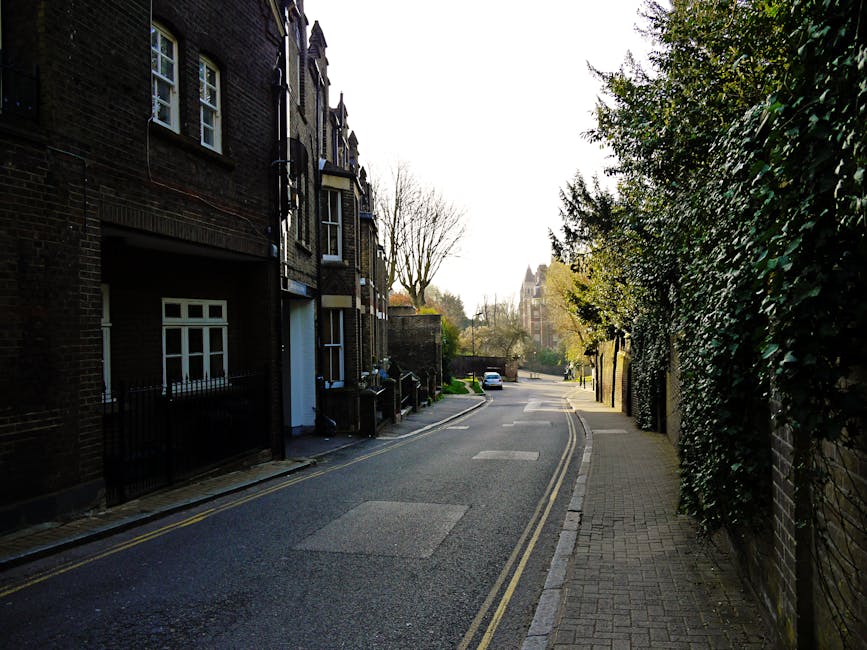 A quiet residential street in High Barnet showing a narrow tarmac road with double yellow line markings along the curbside. On the left, there are dark brick terraced houses with white-framed windows,